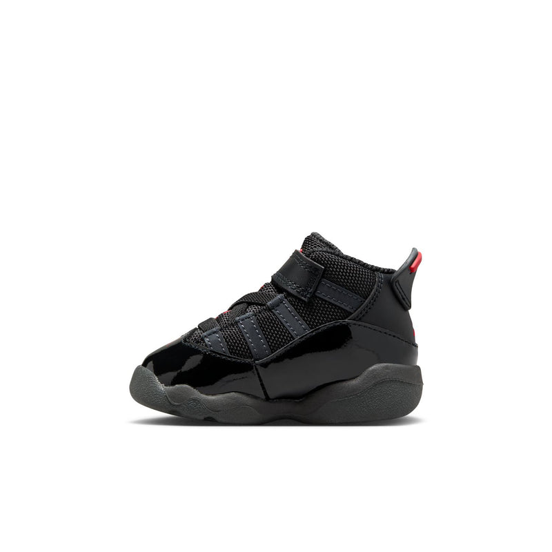 Black toddler sneakers in side profile with textured panels, Velcro straps, and red trim.