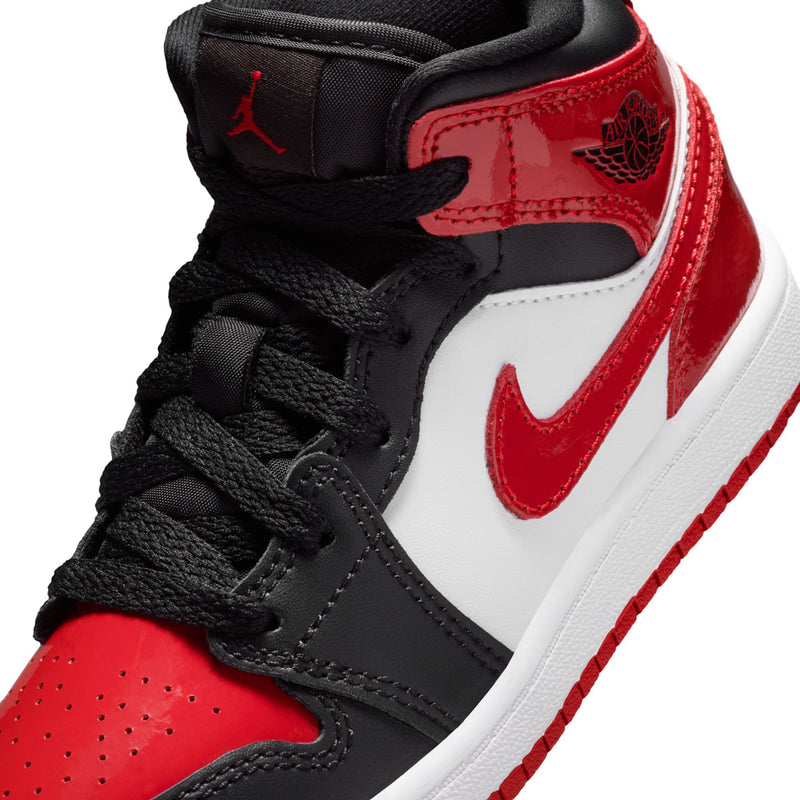 Close-up of kids mid-top sneakers with black laces, white panel, and red overlays.