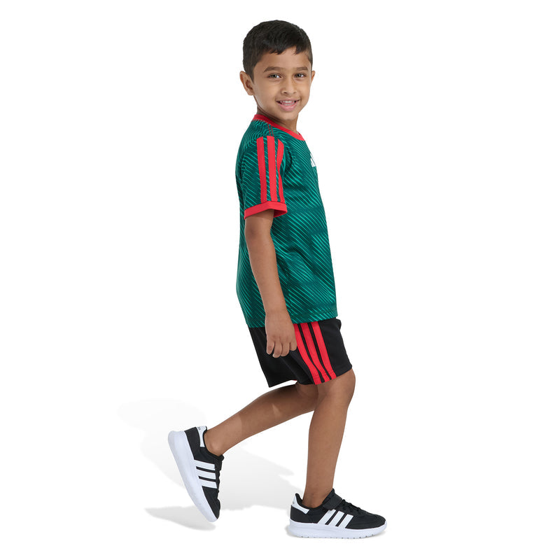 Kids green soccer jersey and black shorts from side profile with red sleeve stripes.