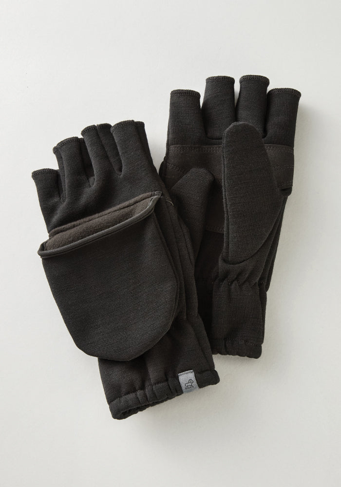 The Cameron Glove Mitten in black from Woolx, designed with a fingerless style and crafted from a Merino wool blend for exceptional warmth, rests on a light surface. These gloves feature an elastic wristband and have a small tag near the edge.