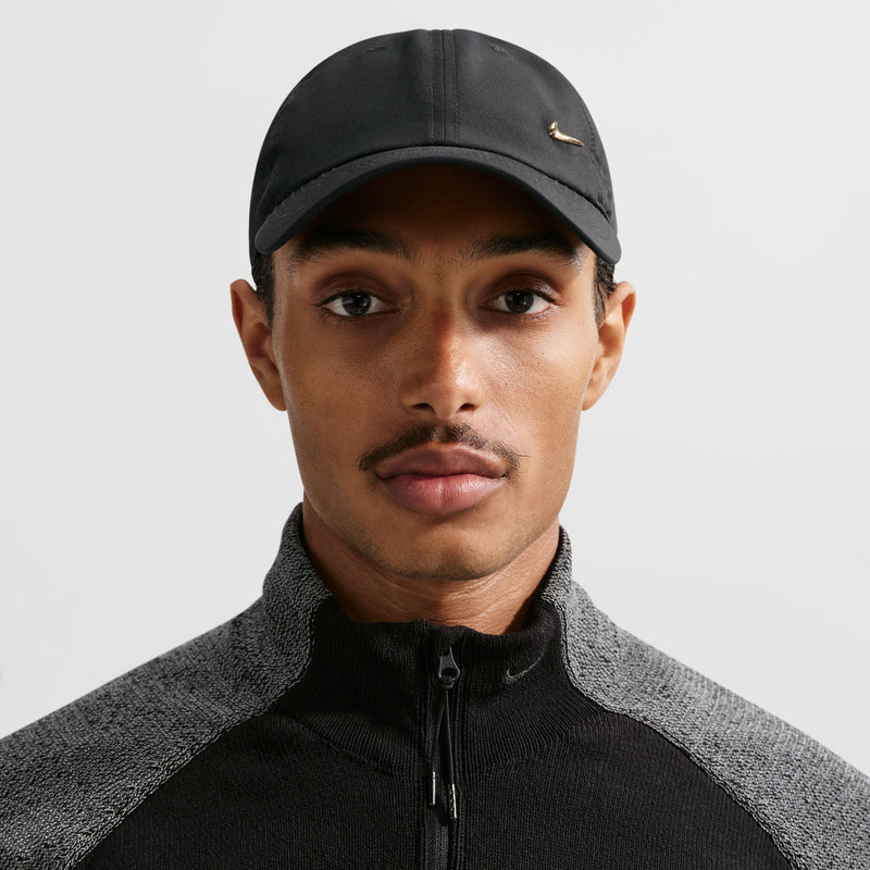 Black strapback cap with metallic gold Nike Swoosh, worn facing forward with curved brim.