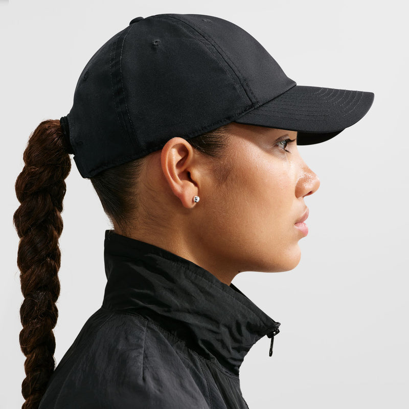 Black strapback cap on head, side profile with metallic gold Nike Swoosh, curved brim.