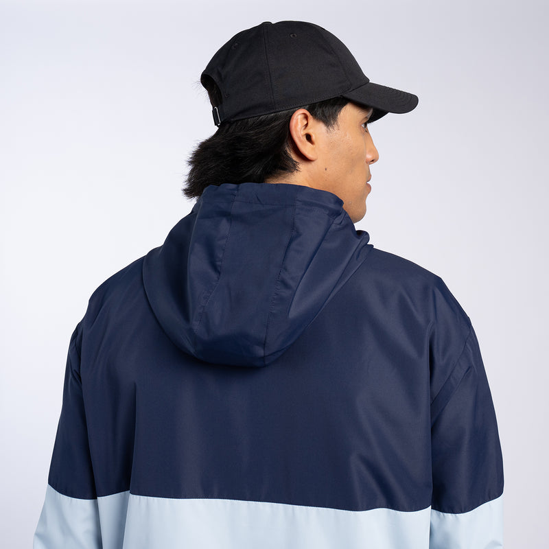 Back view of navy and light-blue windbreaker jacket with hood and colorblock stripe.