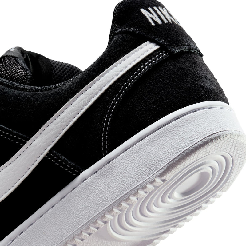 Close-up of black low-top sneaker with white side stripe and white rubber sole edge