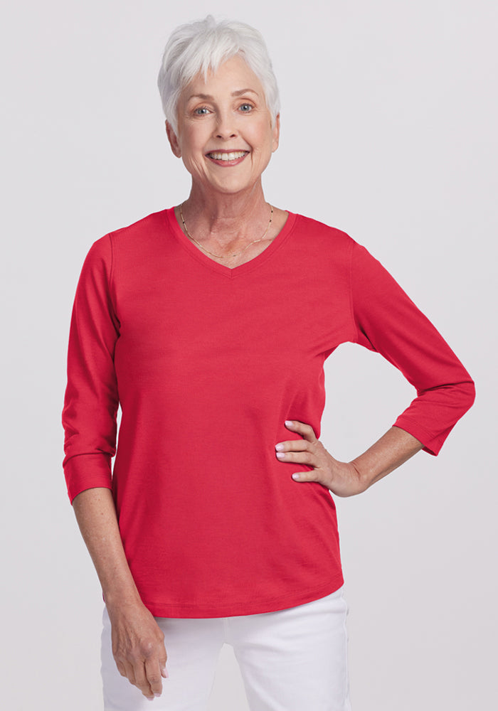 Smiling older woman in a Woolx Elena 3/4 Sleeve V Neck - Berry Ice Pop top and white pants, hand on her hip. | Kathy is 5’9”, wearing a size S