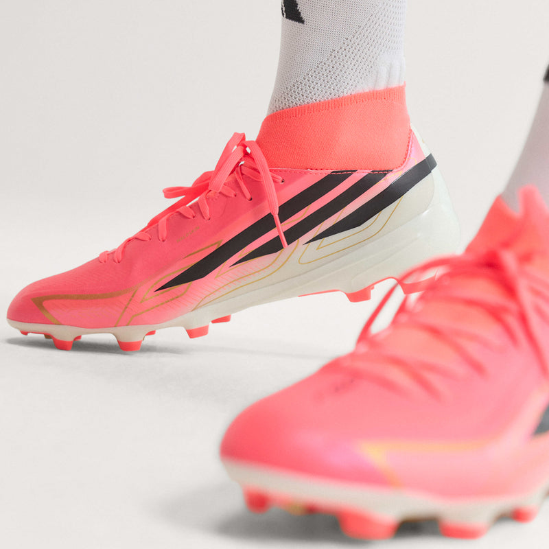 Men's orange-pink soccer cleats side view with black stripes and molded field studs