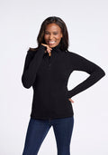A woman with long hair is smiling and posing against a plain white background. She is wearing the Finley Zip Up Sweatshirt in black from Woolx, made of luxurious Australian merino wool, paired with blue jeans. With her left hand on her hip and her right hand touching her face, she effortlessly showcases the flattering look provided by the no-hood design of the sweatshirt. | Keesha is 5’9.5”, wearing a size S
