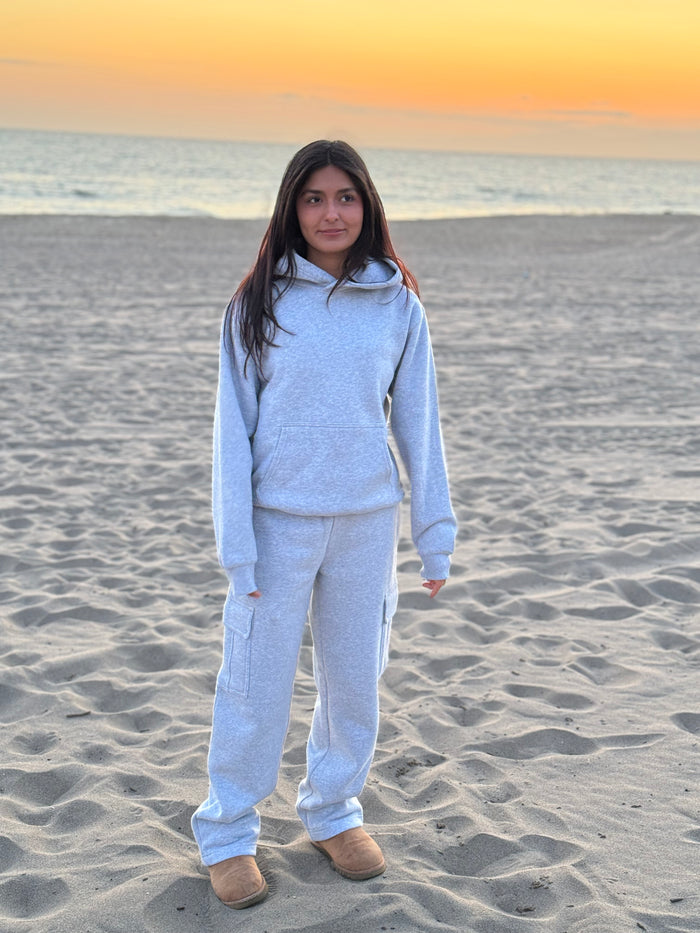 Person wearing gray hoodie and matching cargo pants on the beach at sunset
