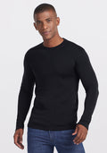 A man wearing the Woolx Glacier Long Sleeve Crew in black and blue jeans stands against a white background, looking at the camera with a slight smile.