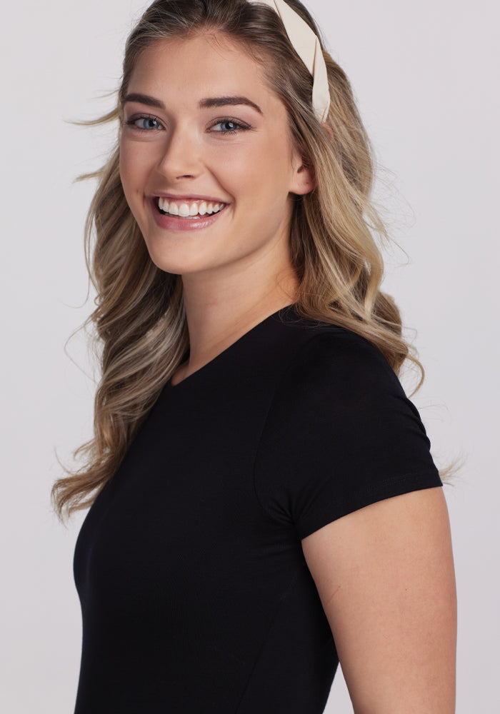 A smiling woman with long blonde hair and a headband wears the Gracie Bodysuit in black by Woolx, set against a plain background.