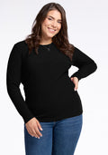 A person with long brown hair smiles at the camera, wearing the Woolx Hadley Ribbed Crew in black and blue jeans. They have one hand on their hip and the other arm relaxed by their side, exuding a luxurious feel against the plain white background. | Juliana is 5'10", wearing a size XL