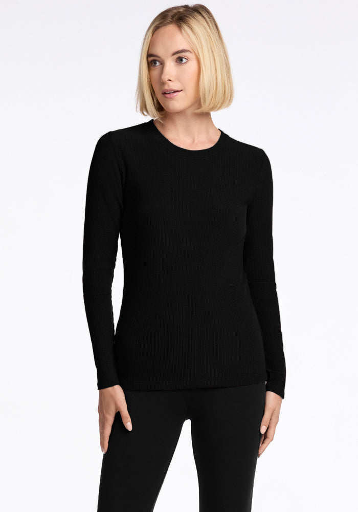 A person with short, blond hair stands against a plain white background, wearing the Hadley Ribbed Crew in black and matching black pants from Woolx. Crafted from luxurious Merino wool, they gaze slightly to the side with a relaxed expression. | Georgia is 5'10", wearing a size XS
