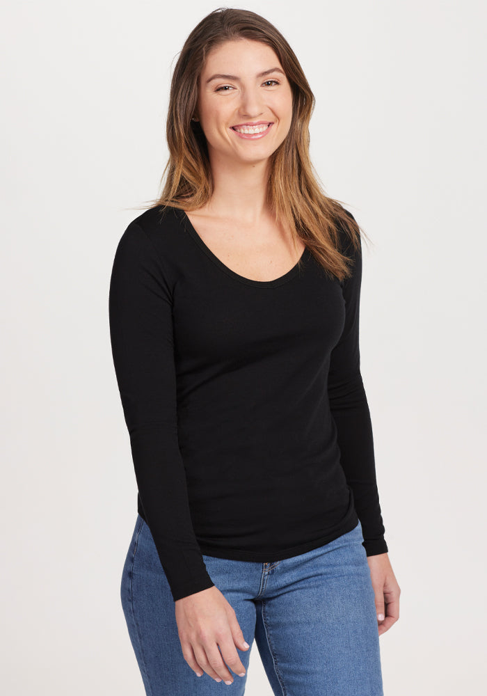 A person with long hair smiles while wearing the odor-resistant, merino wool Layla V Neck Top in black from Woolx, paired with blue jeans. The background is plain white. | Liza is 5'8", wearing a size S