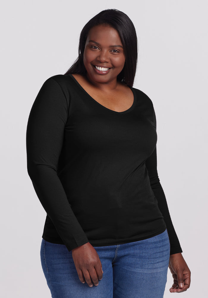 A person in a Woolx Layla V Neck Top - Black, crafted from odor-resistant merino wool, effortlessly pairs it with jeans against a plain grey background, showcasing both style and functionality. | Le'Quita is 5'11", wearing a size XL