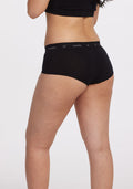 A person is wearing a black top and the Woolx Lila Boy Shorts OLD, crafted from lightweight merino wool, standing against a plain white background. Their back is to the camera, highlighting the fit and style of the clothing.