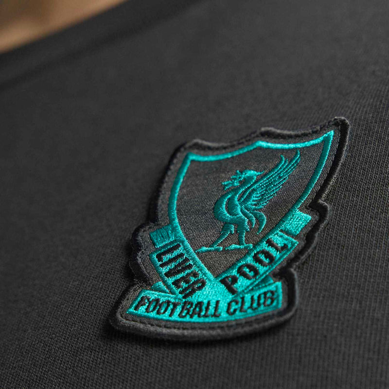 Teal embroidered Liverpool crest patch on black T-shirt, logo detail close-up