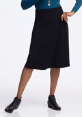A person wearing a blue long-sleeve top and the Woolx Marilyn Flowy Midi Skirt - Black stands confidently in black ankle boots, one hand on their hip. | Keesha is 5’9.5”, wearing a size S