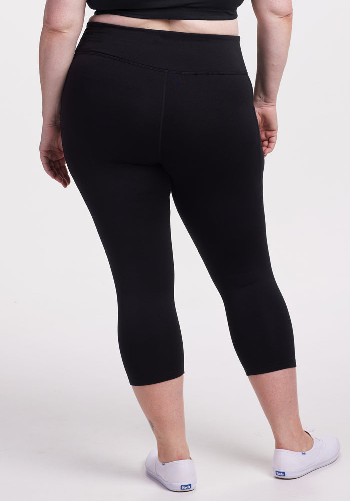 A person is shown from the back, standing against a plain light background, wearing Woolx Merino Flex® McKenna Capris in black and white slip-on shoes.