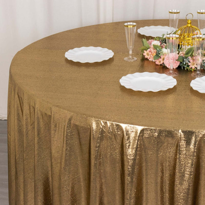 Gold sequin tablecloth on a round table with white plates and floral centerpiece.
