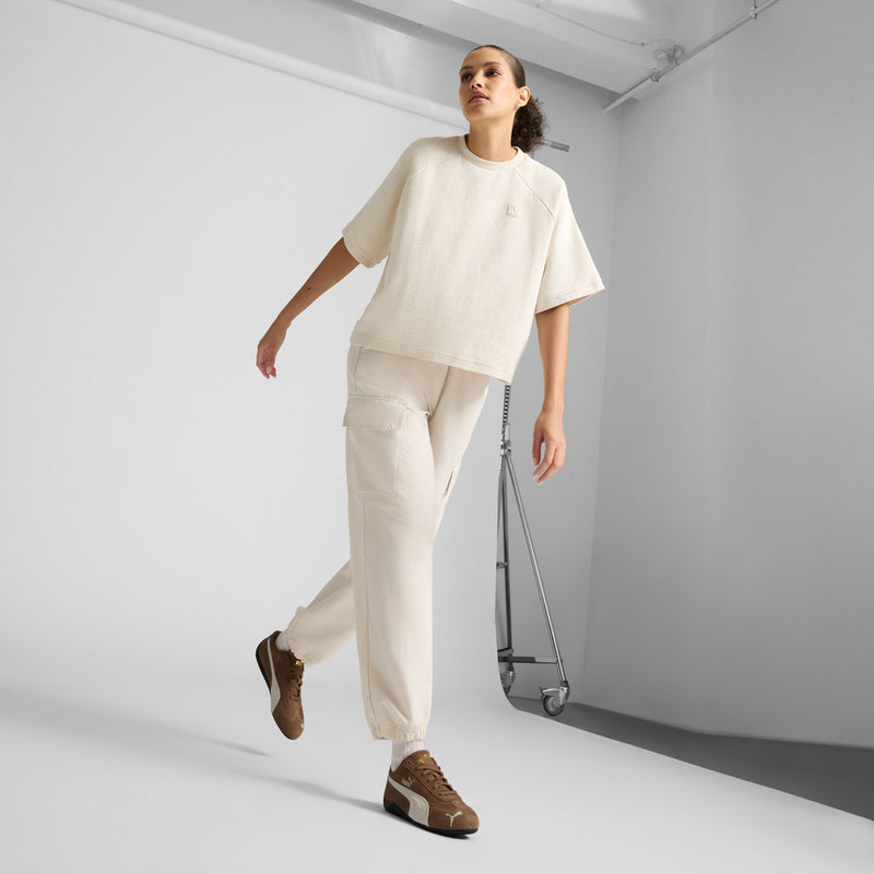 Brown lace-up sneakers with white side stripe, worn with cream pants