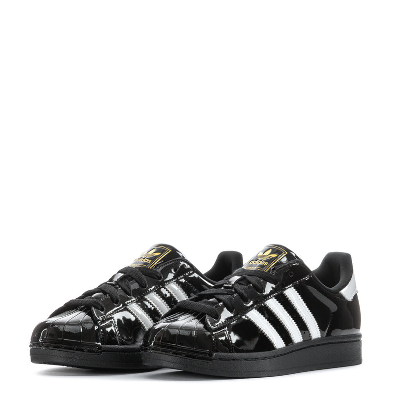 Pair of women’s black patent leather sneakers with white adidas-style stripes and gold heel tabs