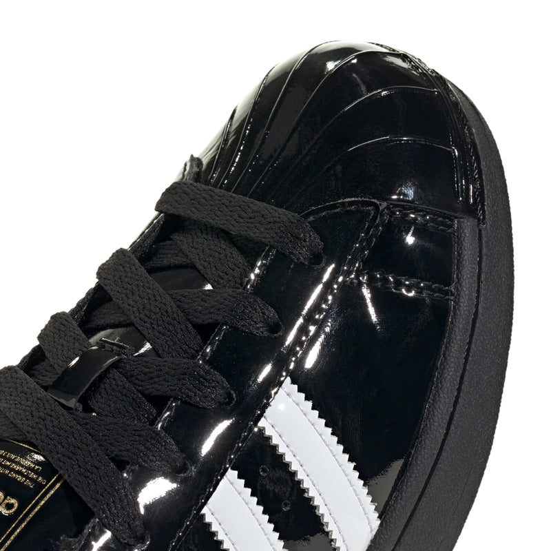Women’s black patent leather sneaker close-up with white stripe detail and black laces