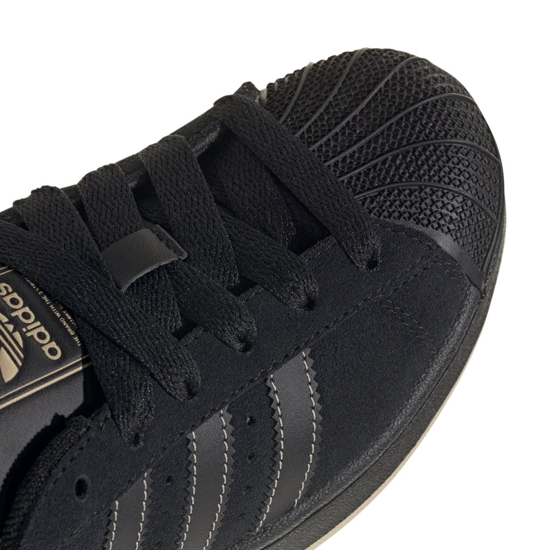 Youth black sneaker upper close-up with lace area and stitched three-stripe overlays.