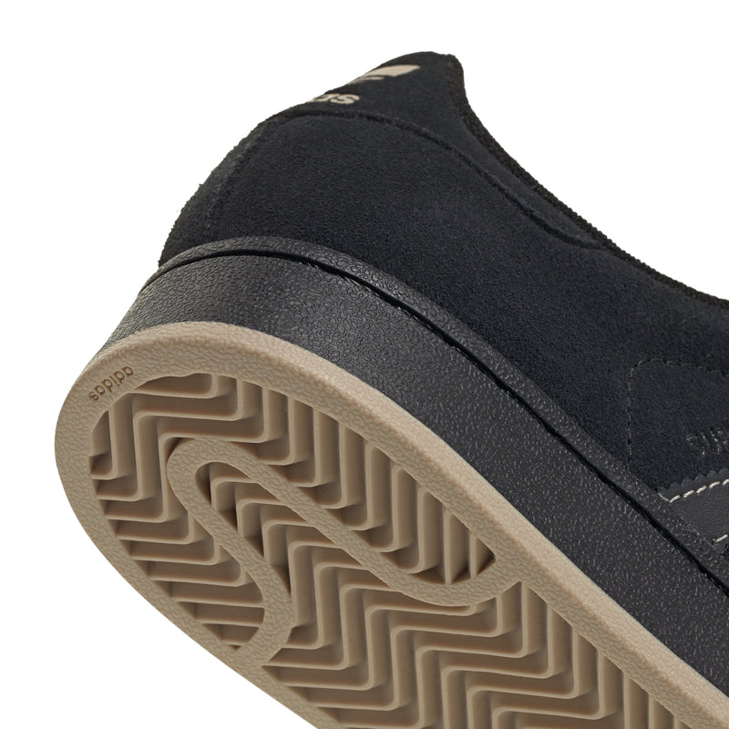 Youth black sneaker outsole tread close-up with textured rubber pattern.