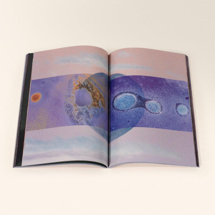 Open book displaying a two-page spread with abstract celestial imagery in purple blue and gold