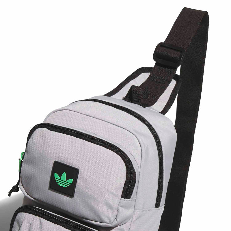 Light grey crossbody sling bag with adjustable black strap and front patch logo