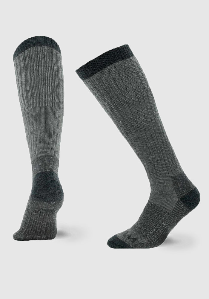 Displayed against a plain background, the Woolx Extreme Extra Cushion Over the Calf socks in Charcoal Heather are crafted with Merino wool for exceptional insulation. One sock stands upright showcasing its full length, while the other is angled to reveal its sole and heel. Both feature darker bands at the top, heel, and toe areas, making them ideal for cold-weather wear.