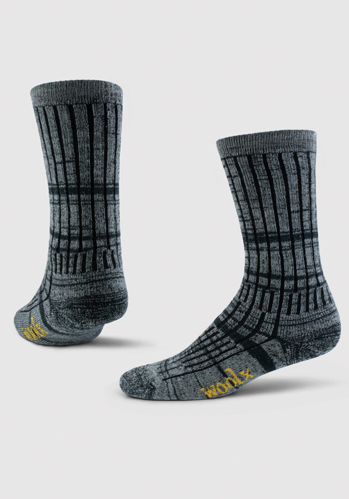 Displayed are two Joey Socks - Dark Navy Marled by Woolx, featuring a sophisticated dark navy merino wool design with subtle grid patterns. One sock is upright, and the other is angled, showcasing the yellow text near the toes set against a white background. These socks are an ideal cozy and warm choice for your next adventure.